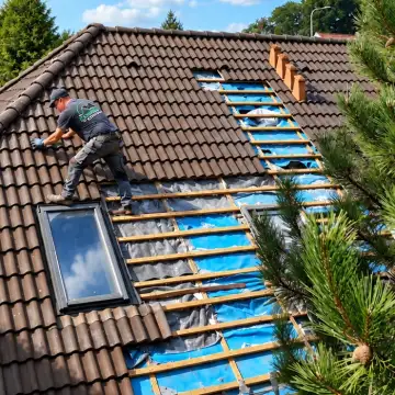 Dekarz układa nową membranę i łaty na otwartej połaci